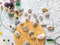 Kamienie z numerami, kostki do gry i talizmany na tle wykresów astrologicznych. Wibracja dnia 5 jest widoczna na jednym z kamieni.