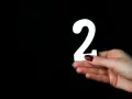 Dłoń z ciemnoczerwonym lakierem trzyma białą cyfrę 2. Co oznacza liczba 2?