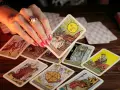 Dłoń z pierścionkiem wybiera kartę Słońce z talii tarot. Rozłożony krzyż celtycki tarot zapowiada przyszłość.