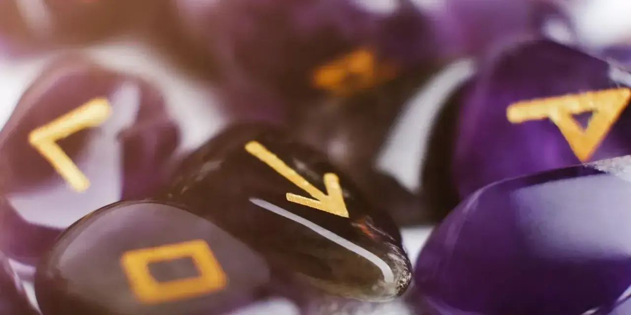 Kamienie z runami, w tym symbol przypominający numerologiczną 1, tworzą mistyczną kompozycję.