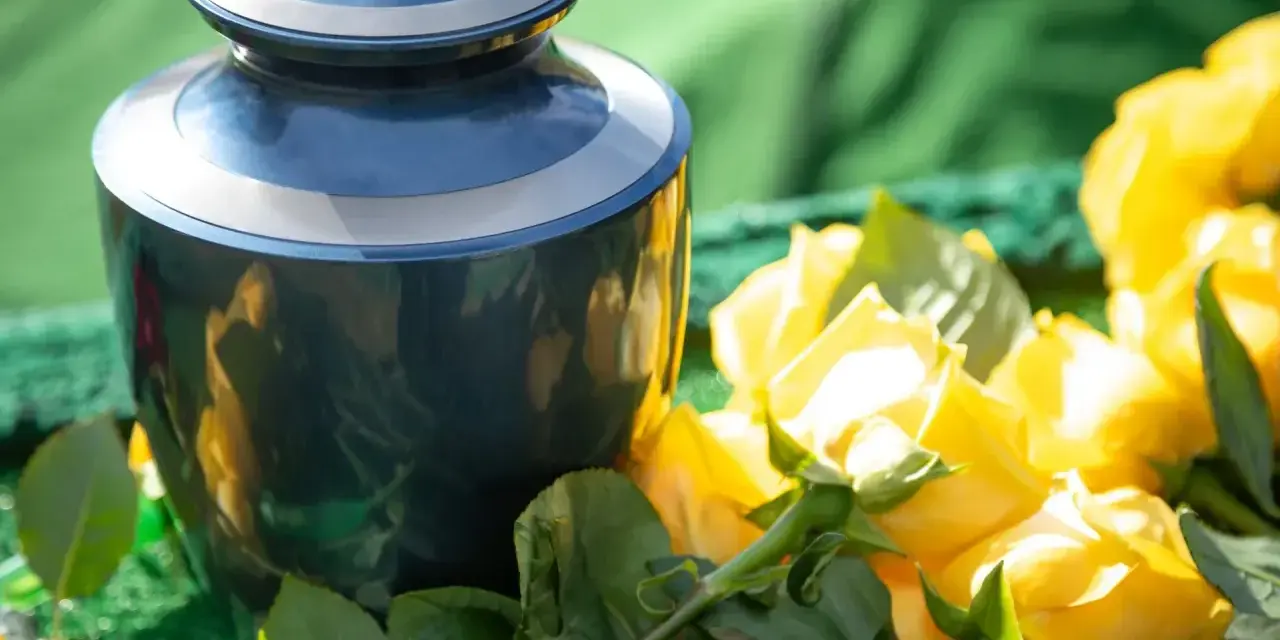 Granatowa urna pogrzebowa obok bukietu żółtych róż. Kwiaty te, zgodnie z przesądami pogrzebowymi, symbolizują pamięć i szacunek.
